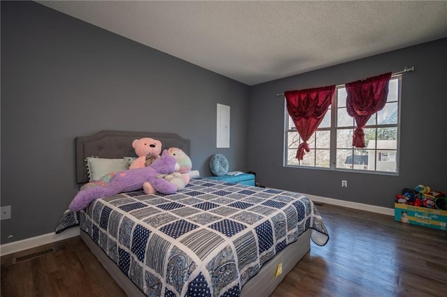 bedroom with visible vents, a textured ceiling, baseboards, and wood finished floors