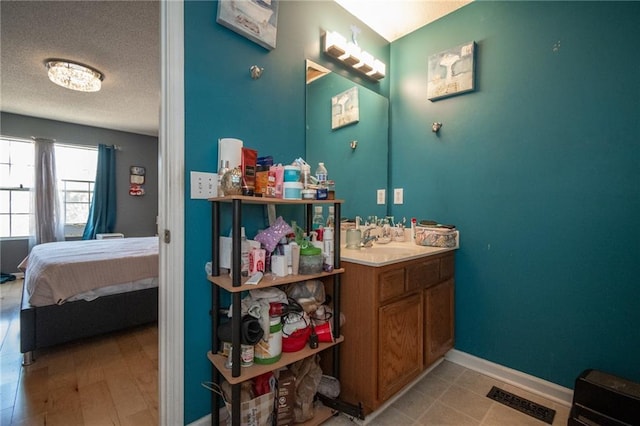 ensuite bathroom featuring a textured ceiling, ensuite bathroom, vanity, visible vents, and baseboards