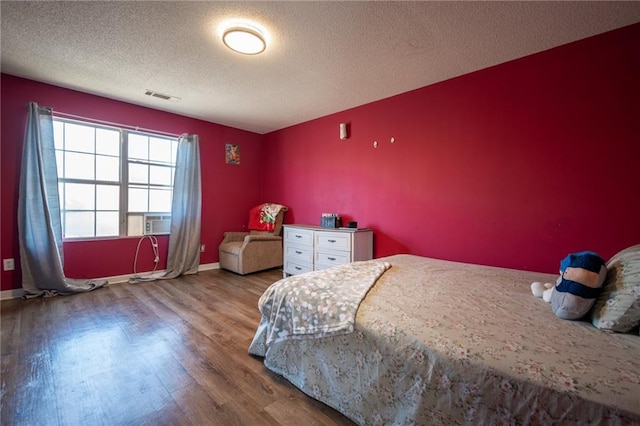 bedroom with visible vents, a textured ceiling, baseboards, and wood finished floors