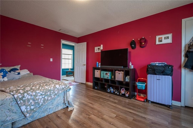 bedroom featuring visible vents, an accent wall, a textured ceiling, wood finished floors, and baseboards