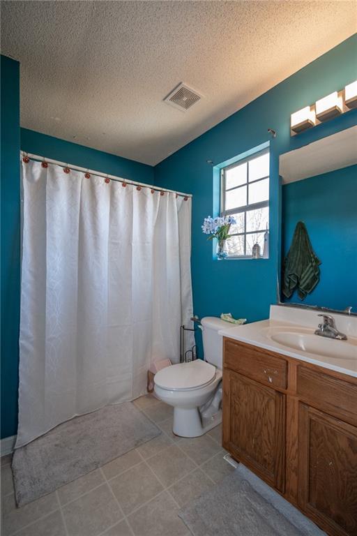 full bathroom featuring visible vents, toilet, a textured ceiling, vanity, and tile patterned floors