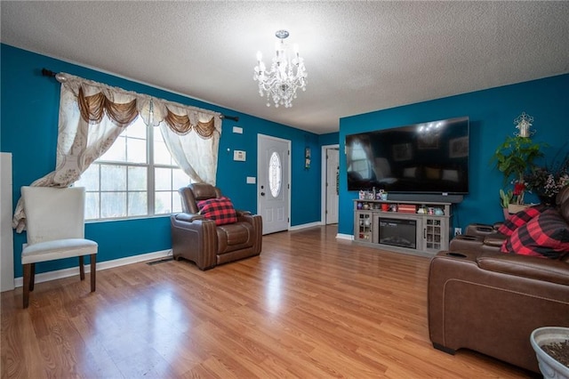 living room featuring a chandelier, a glass covered fireplace, a textured ceiling, and wood finished floors