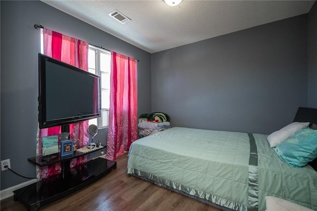 bedroom with visible vents, a textured ceiling, and wood finished floors