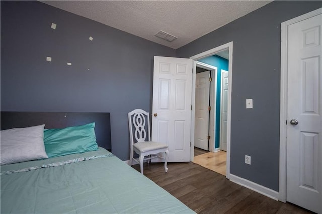 bedroom with baseboards, a textured ceiling, visible vents, and wood finished floors