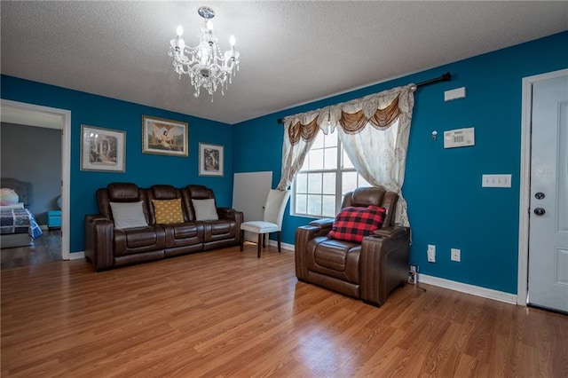 living room with baseboards, a textured ceiling, wood finished floors, and a notable chandelier