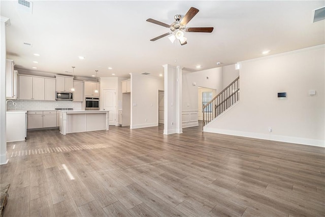 unfurnished living room featuring sink, crown molding, light hardwood / wood-style floors, and ceiling fan