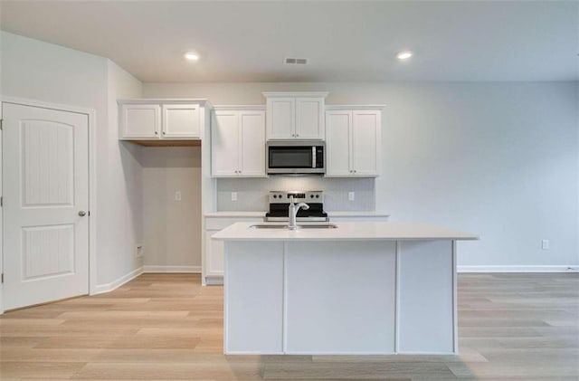 kitchen with sink, white cabinetry, a kitchen island with sink, light hardwood / wood-style floors, and stainless steel appliances