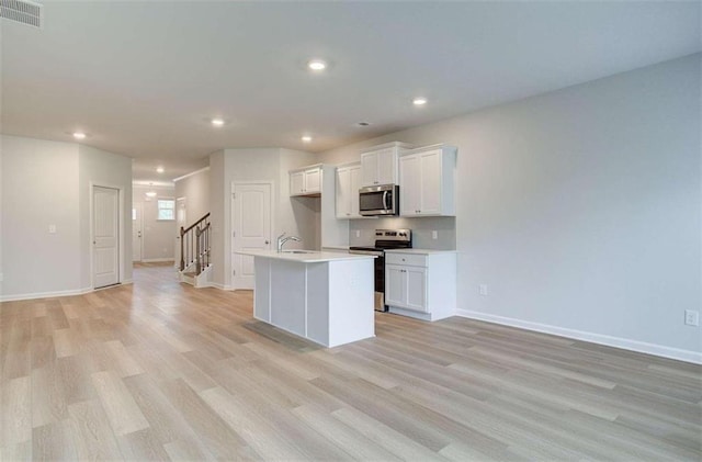 kitchen with white cabinets, stainless steel appliances, light hardwood / wood-style flooring, and a kitchen island with sink