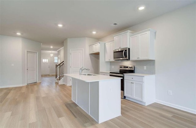 kitchen featuring white cabinets, stainless steel appliances, sink, and an island with sink