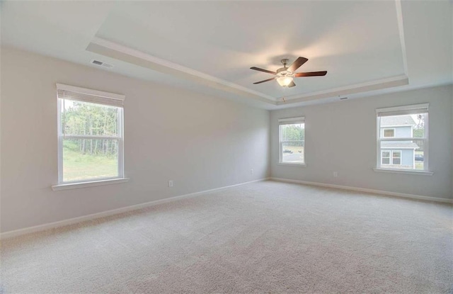 empty room featuring ceiling fan, light colored carpet, and a tray ceiling