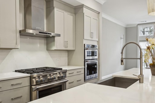 kitchen featuring wall chimney range hood, light countertops, a sink, and appliances with stainless steel finishes