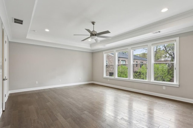 unfurnished room with a raised ceiling, dark wood finished floors, ceiling fan, and visible vents