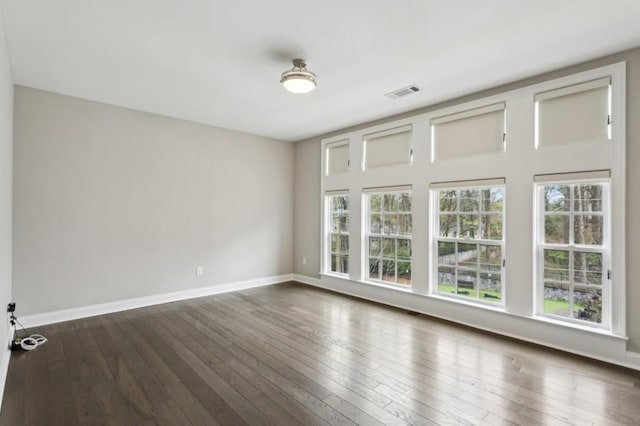 empty room featuring a wealth of natural light, visible vents, baseboards, and dark wood-style flooring