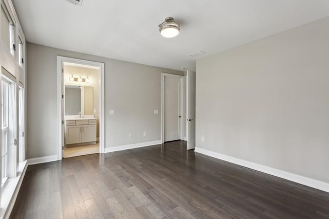 unfurnished bedroom with baseboards, ensuite bathroom, and dark wood finished floors