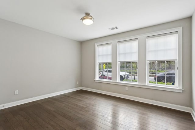 unfurnished room with baseboards, a wealth of natural light, visible vents, and dark wood-type flooring