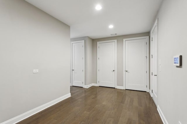 unfurnished bedroom featuring baseboards, multiple closets, wood finished floors, and recessed lighting
