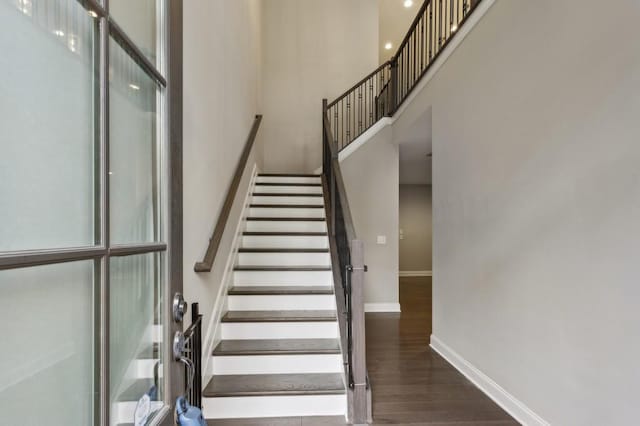 stairway featuring baseboards, a towering ceiling, and wood finished floors