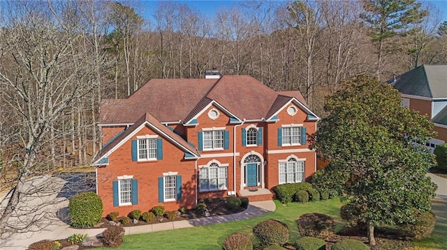 georgian-style home featuring a front lawn, brick siding, and a chimney