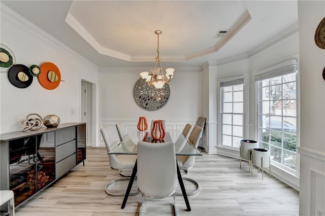 dining room featuring light wood-style flooring, a tray ceiling, crown molding, wainscoting, and a chandelier