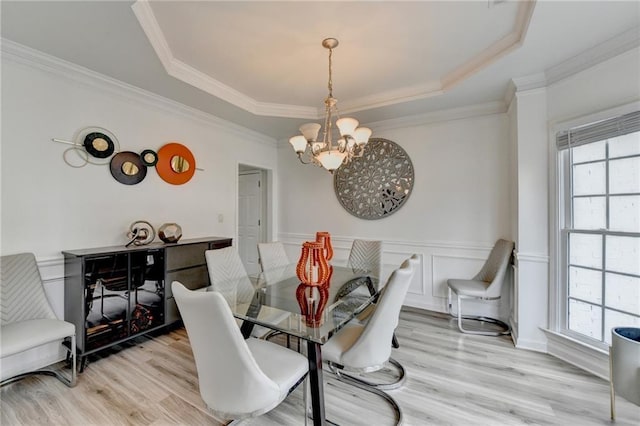 dining space with wainscoting, a notable chandelier, light wood-style flooring, and a tray ceiling