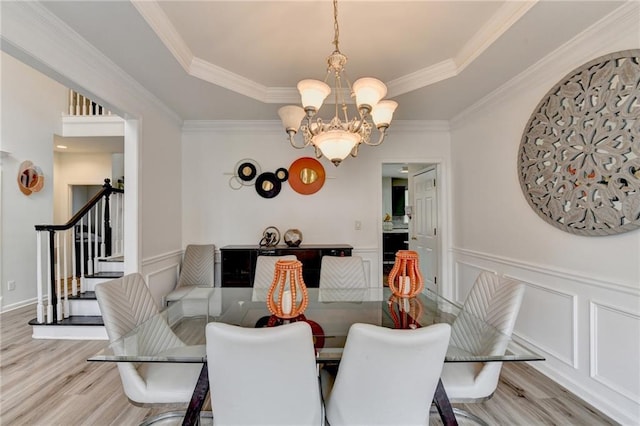 dining space with a tray ceiling, stairway, a chandelier, and light wood-style flooring