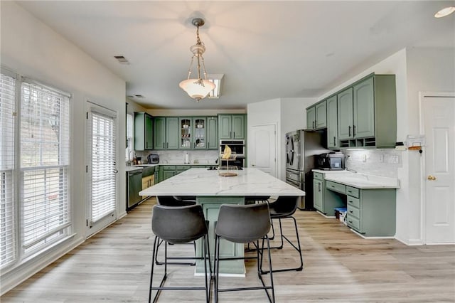 kitchen with visible vents, green cabinetry, appliances with stainless steel finishes, a kitchen bar, and light wood-type flooring