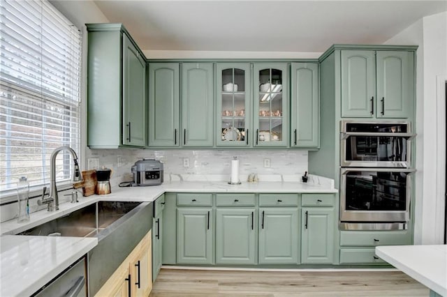 kitchen featuring a sink, light stone counters, tasteful backsplash, stainless steel appliances, and green cabinets