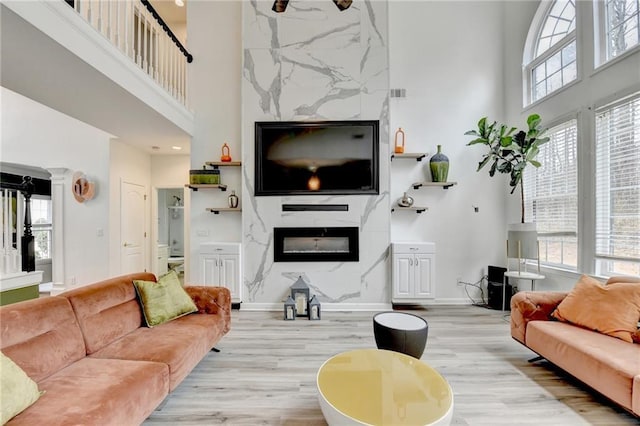 living room featuring light wood-style flooring, a fireplace, baseboards, and a towering ceiling