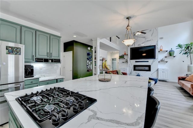 kitchen featuring freestanding refrigerator, black gas stovetop, green cabinets, and light stone counters