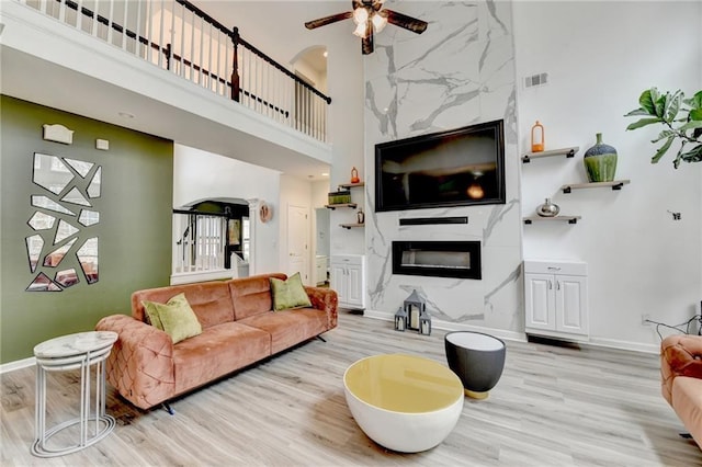 living area with a high end fireplace, a high ceiling, light wood finished floors, baseboards, and ceiling fan