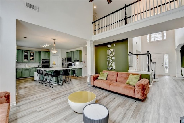 living room with visible vents, a high ceiling, stairs, and decorative columns