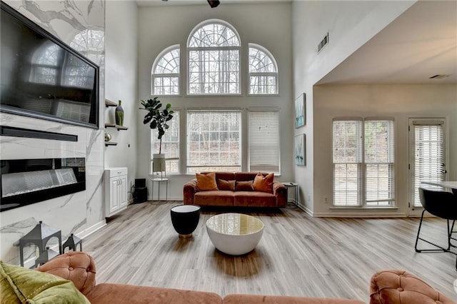 living area with a wealth of natural light, visible vents, light wood-type flooring, and a towering ceiling