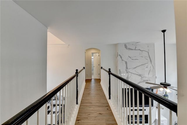 corridor featuring arched walkways, an upstairs landing, and light wood-style flooring