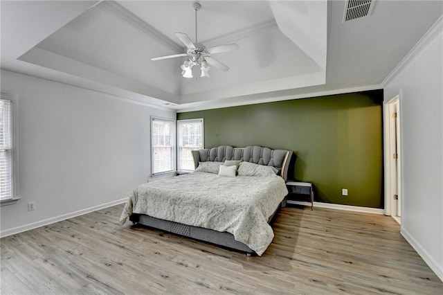 bedroom featuring a tray ceiling, baseboards, visible vents, and wood finished floors