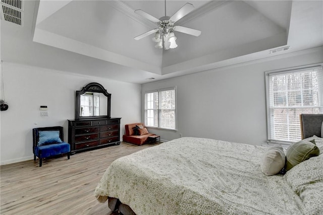 bedroom with a tray ceiling, light wood-style floors, and visible vents