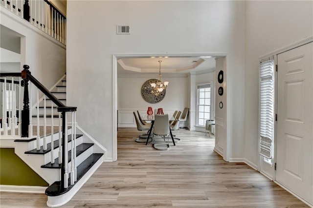 foyer entrance featuring a raised ceiling, crown molding, light wood-style floors, and visible vents