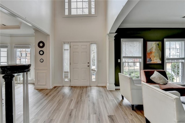 entrance foyer with baseboards, crown molding, light wood-style floors, and decorative columns