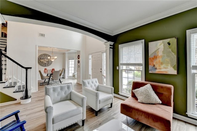 living area with stairway, wood finished floors, ornate columns, crown molding, and a chandelier