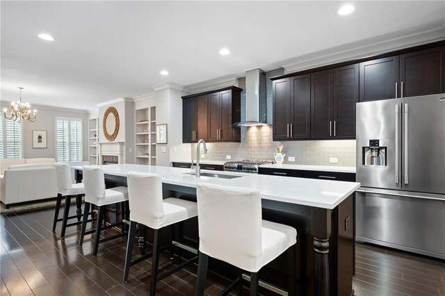 kitchen featuring a kitchen island with sink, stainless steel appliances, wall chimney exhaust hood, and pendant lighting