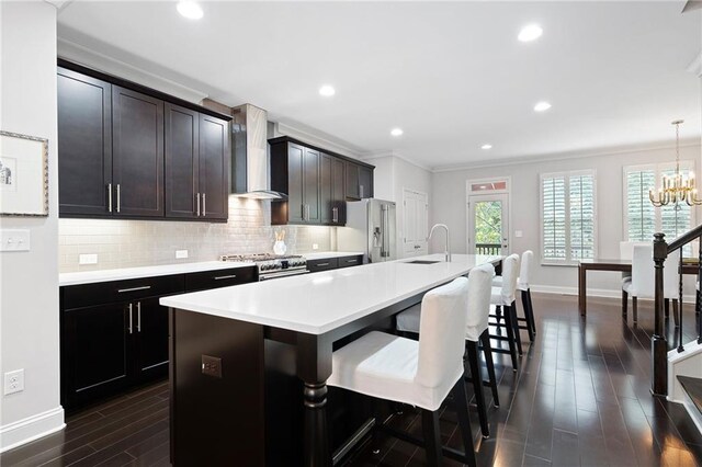 kitchen featuring stainless steel appliances, wall chimney exhaust hood, decorative light fixtures, a kitchen island with sink, and dark hardwood / wood-style flooring