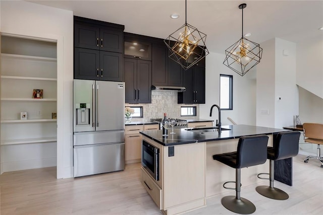 kitchen featuring high end refrigerator, a sink, built in microwave, light wood-style floors, and a breakfast bar