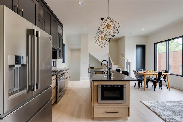 kitchen with high end appliances, a sink, light wood-style flooring, an island with sink, and recessed lighting