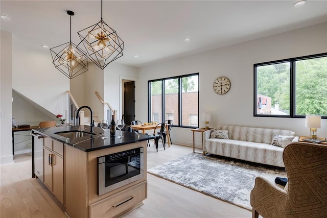 kitchen with a sink, light wood-style flooring, open floor plan, a chandelier, and an island with sink