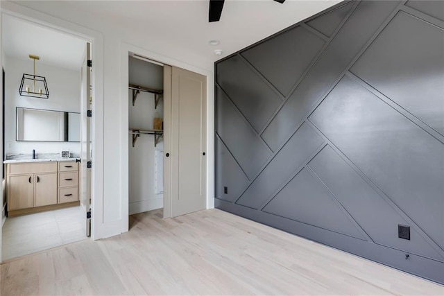 unfurnished bedroom featuring a closet, ensuite bath, light wood-type flooring, and a decorative wall