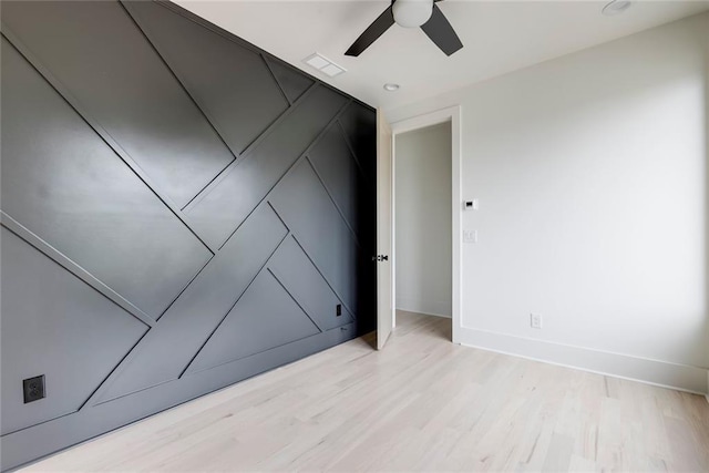 spare room featuring ceiling fan, light wood-style floors, baseboards, and a decorative wall