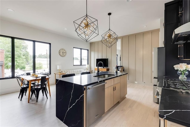 kitchen featuring a sink, dishwasher, light wood-type flooring, refrigerator, and a kitchen island with sink