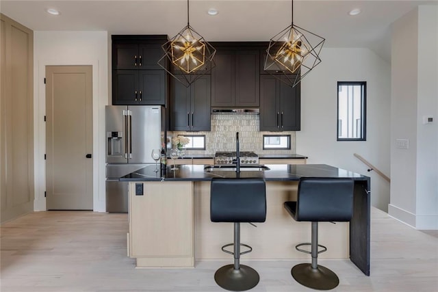 kitchen with stainless steel refrigerator with ice dispenser, under cabinet range hood, light wood finished floors, decorative backsplash, and dark countertops
