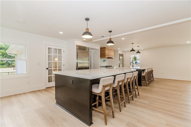 kitchen with light wood-type flooring, a spacious island, built in refrigerator, hanging light fixtures, and a breakfast bar area