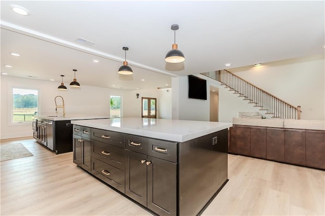 kitchen featuring a kitchen island, sink, light wood-type flooring, and hanging light fixtures