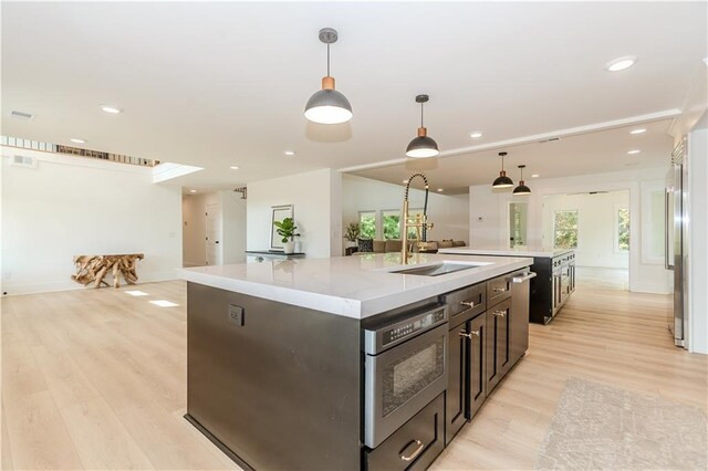 kitchen featuring sink, hanging light fixtures, oven, an island with sink, and light wood-type flooring